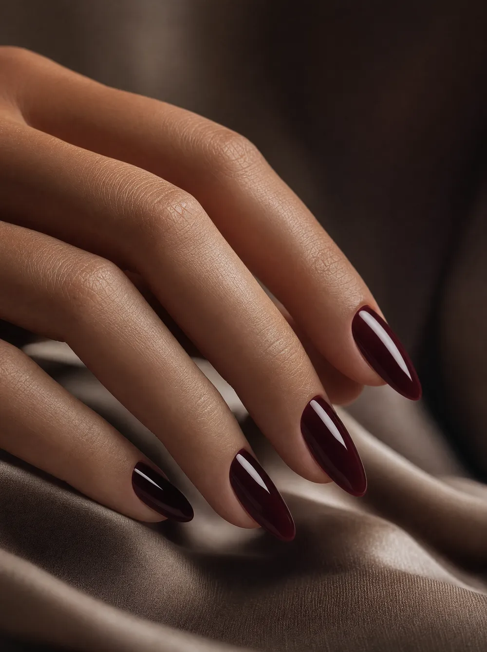Manicure glossy burgundy su unghie a mandorla, luce laterale
