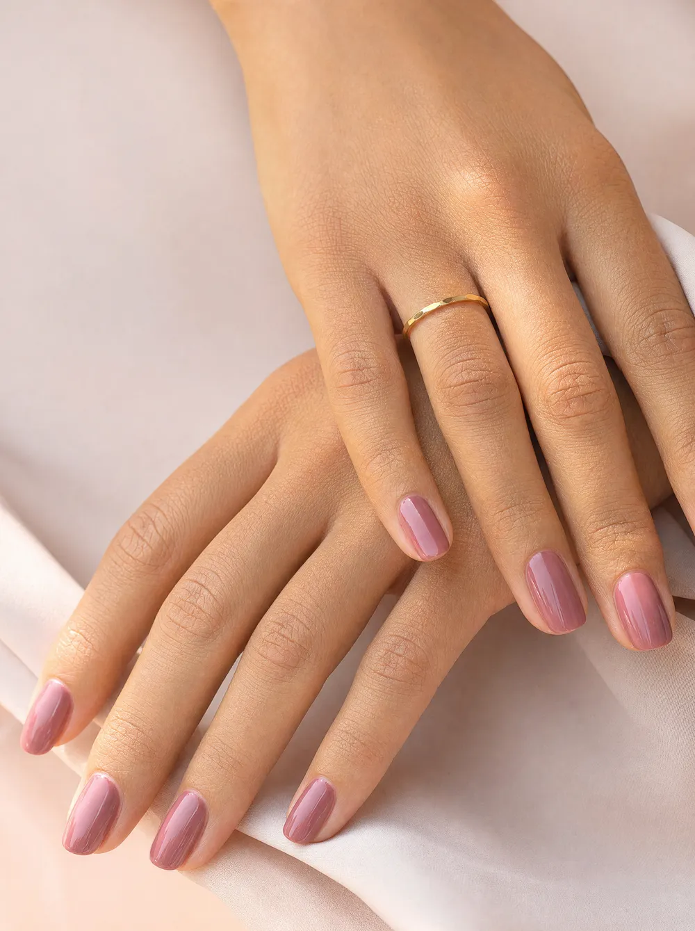 Due mani sovrapposte con manicure dusty rose e anello dorato